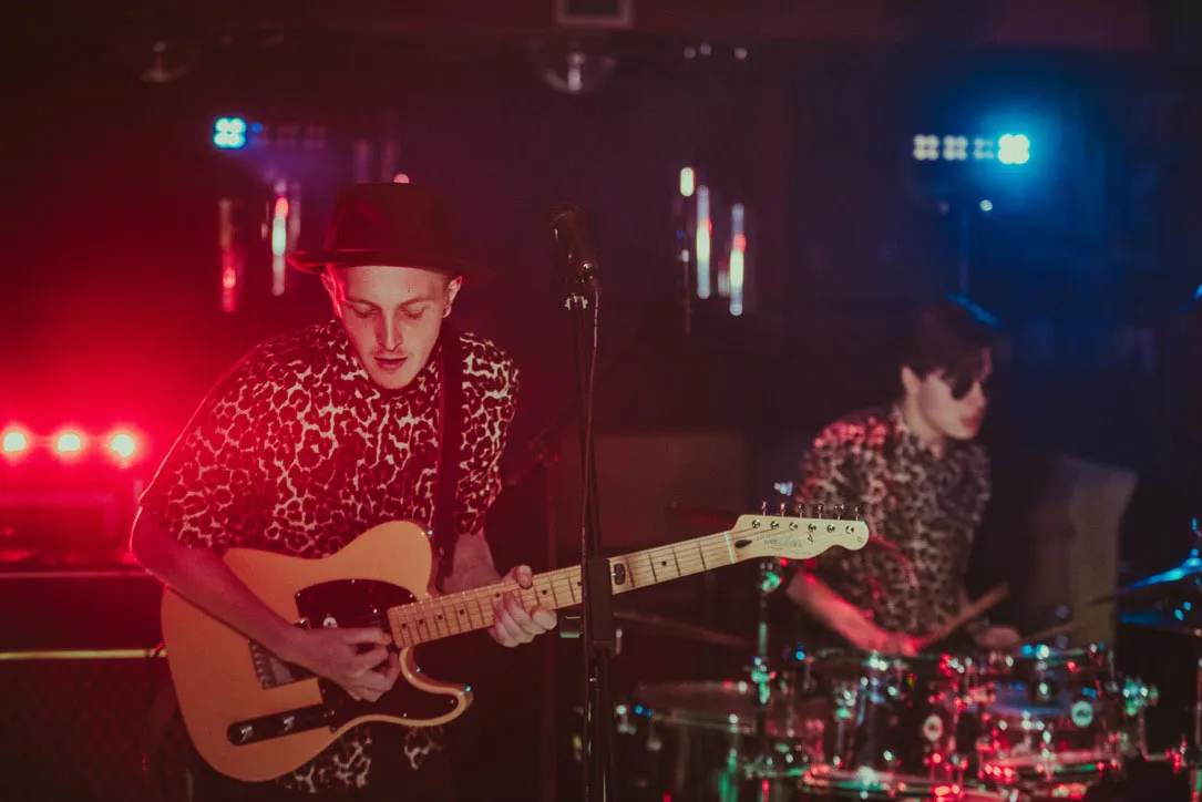 Band member playing electric guitar under red stage lights