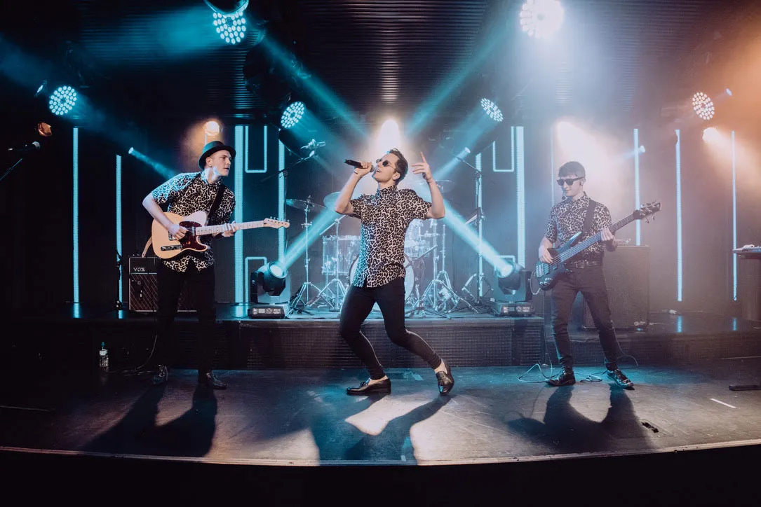Full band performing live on stage with blue spotlights